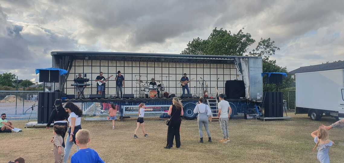 A trailer stage with a band playing on it in front of a small group of people.