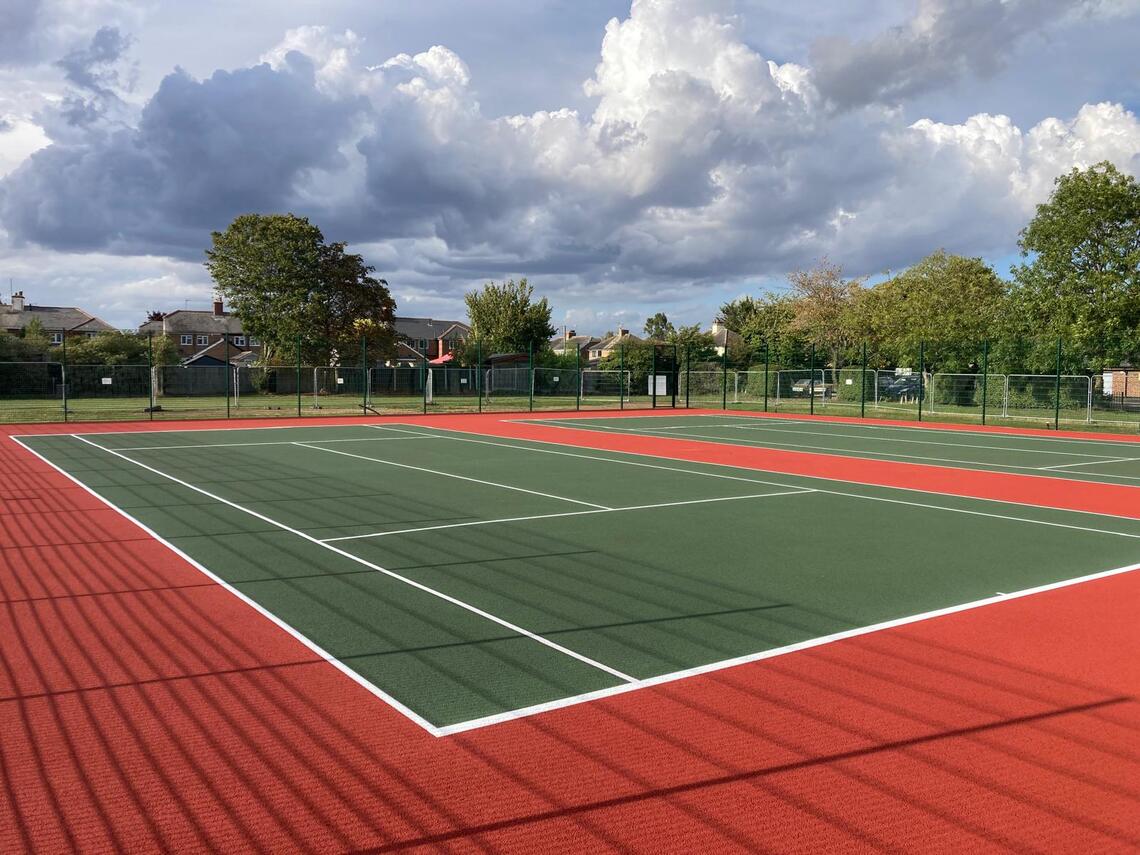 Wide angle photo of green tennis court with white court markings and red asphalt surround