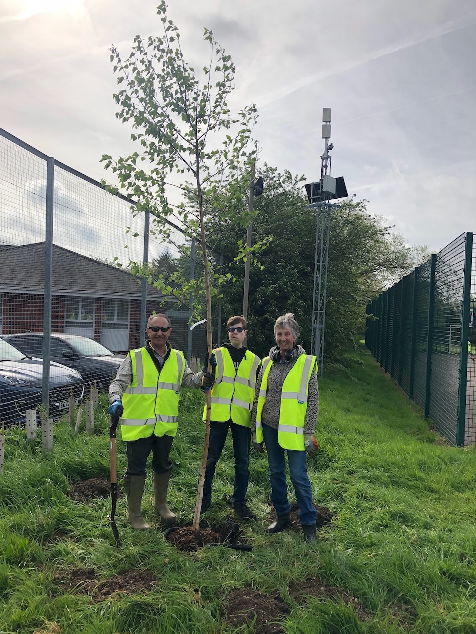three gardeners in hi-vis vests standing with their tools after a hard days work